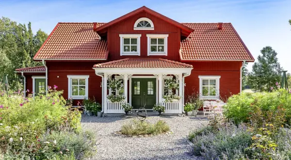 Vackert rött hus med vita detaljer, en veranda och en blomstrande trädgård. Ett perfekt exempel på att **bygga hus i gammal stil**.