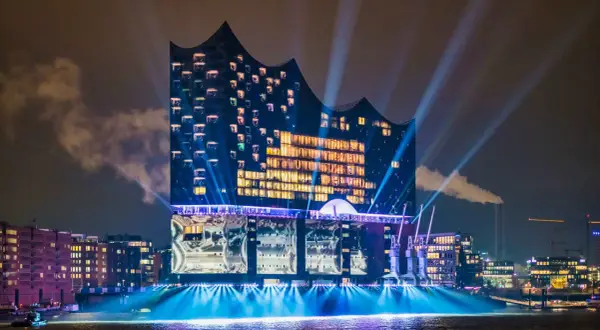 Elbphilharmonie, konserthus Hamburg, badar i ljus och strålkastare över vattnet en mörk kväll.