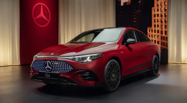 Elegancki, czerwony nowy Mercedes CLA z podświetlanym grillem i czarnymi felgami stoi na ciemnym tle z miejskim krajobrazem w tle.