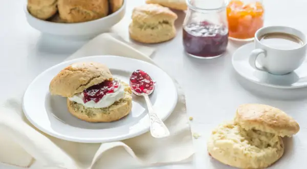 Ein Scone mit Clotted Cream und Marmelade, daneben eine Tasse Kaffee und weitere Scones.