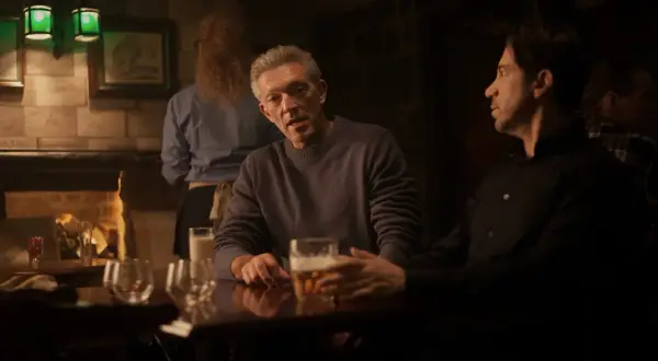 Besetzung von Damaged: Vincent Cassel und Reda Kateb sitzen in einer dunklen Bar bei Bier.