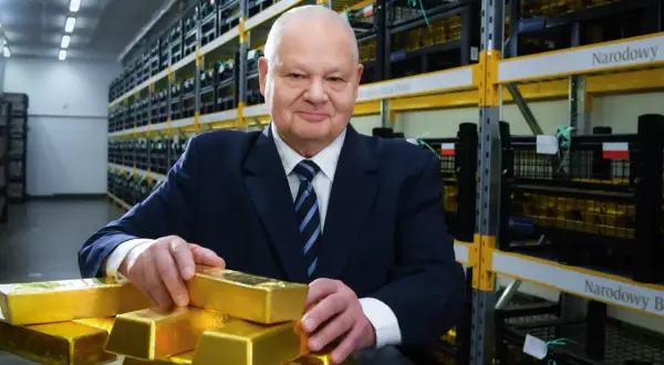 Mężczyzna w garniturze w magazynie Narodowego Banku Polskiego pokazuje sztabki złota, sugerując, ile złota ma Polska.