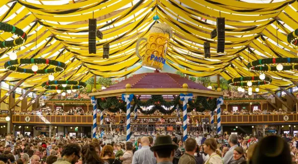 Festa della birra a Monaco: un'enorme folla festeggia sotto un tendone decorato con festoni gialli e neri, dominato da un gigantesco boccale di birra.