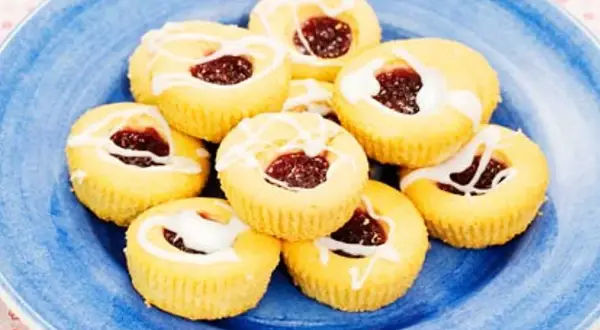 Hallongrottor recept: små, runda kakor med hallonsylt i mitten och glasyr på en blå tallrik.