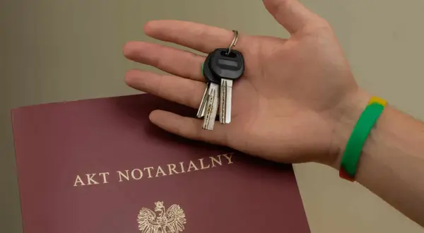 Dłoń trzyma klucze do nowego domu, obok leży akt notarialny. To symboliczny moment podpisania umowy przedwstępnej.