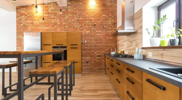 Cocina estilo industrial con pared de ladrillo visto, muebles de madera, encimera oscura y una isla con bancos.
