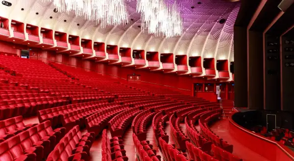 Interno di un teatro moderno con file di poltrone rosse e un soffitto decorato. Uno dei teatri più grandi d'Italia, pronto ad accogliere il pubblico.