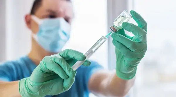 Medyk w zielonych rękawiczkach pobiera płyn do strzykawki, przygotowując szczepionkę na tężec.