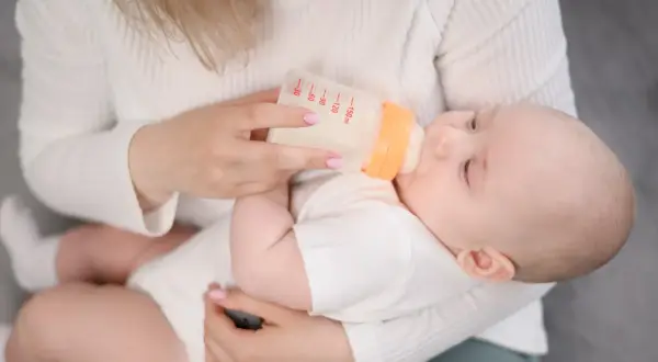 Mama karmi dziecko butelką z mlekiem. Na butelce widać miarkę, jak przy wycofanym mleku Bebilon.