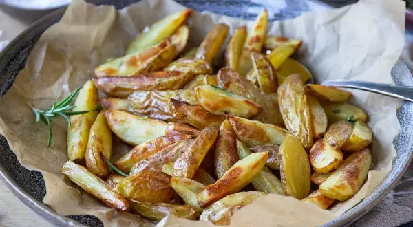 Krispiga klyftpotatis i airfryer, gyllene och redo att serveras med en kvist rosmarin.