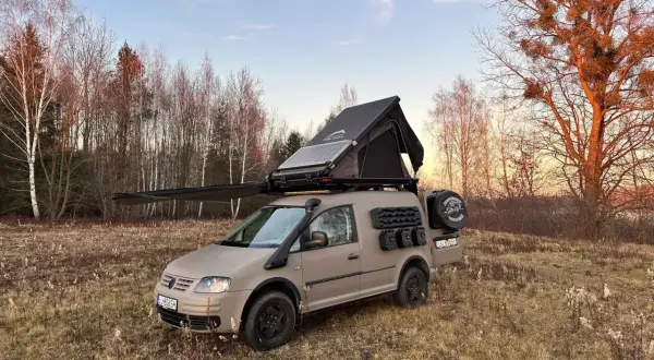 Zmodyfikowany caddy kamper z namiotem dachowym i panelem słonecznym gotowy na przygodę w lesie.