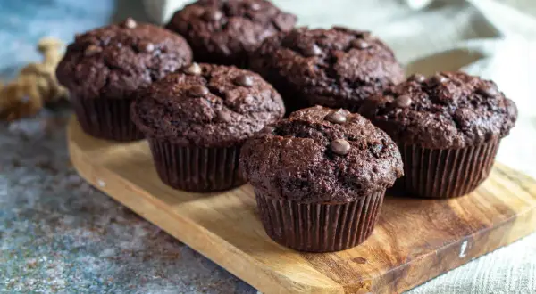 Muffins med chokladbitar, saftiga och mörka, ligger uppradade på en träbricka. Perfekta för fikat!