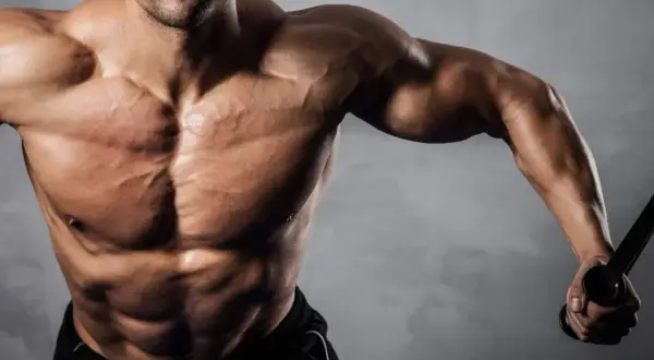 Uomo muscoloso con addominali scolpiti, che si allena con cavi. Ideale per chi cerca recupero e crescita muscolare con aminoacidi dopo allenamento.