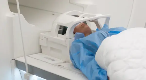 Pacjent leży w aparacie do rezonansu magnetycznego. Czy rezonans głowy obejmuje uszy? Tak, specjalna cewka jest umieszczona wokół głowy, zakrywając uszy.