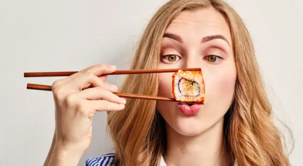 Kobieta z pałeczkami trzyma sushi przed ustami, zastanawiając się, czy sushi jest kaloryczne.