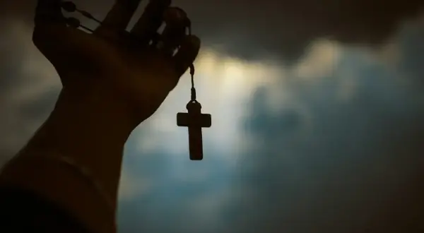 Dłoń trzyma paciorki różańca z krzyżem. Czy to symbol wiary, czy wątpliwości agnostyka, a może wyraz buntu ateisty?