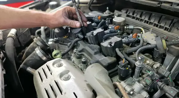 Mécanicien utilisant une visseuse pour changer les bougies d'allumage essence. Un moteur de voiture est visible.