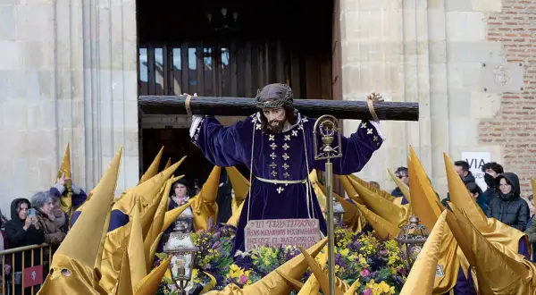 Imagen de una **procesión Miércoles Santo**. Una figura de Jesús carga la cruz, rodeada de nazarenos con túnicas moradas y capirotes dorados.
