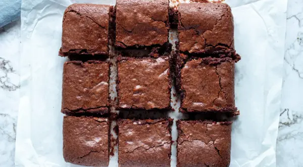 Nio saftiga bitar av glutenfri brownie ligger uppskurna på bakplåtspapper.