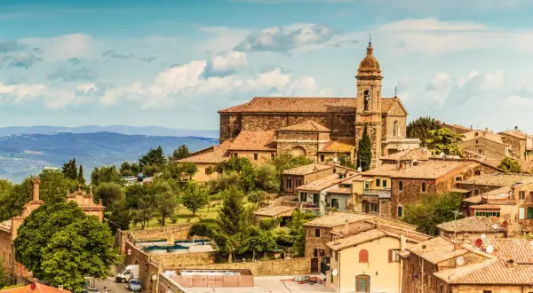 Panoramic view of Montalcino, Italy, with terracotta roofs, a church, and rolling hills under a blue sky.