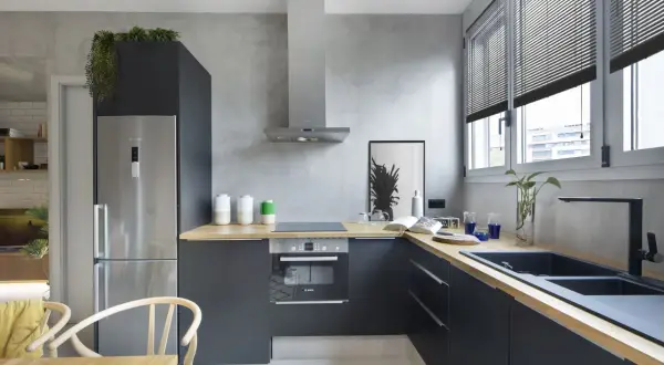 Cocina moderna con paredes de microcemento, muebles oscuros, encimera de madera y electrodomésticos de acero inoxidable.