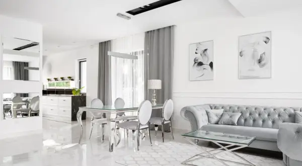 Eleganckie, nowoczesne wnętrze w stylu glamour. Błyszczące płytki, szara sofa i szklany stół tworzą luksusową atmosferę.