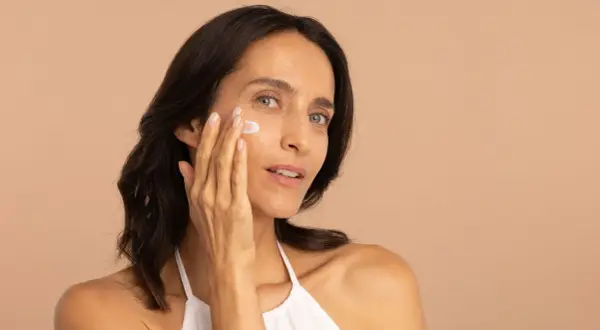 Une femme applique une crème sur son visage, profitant des bienfaits de l'hydratation pour une peau radieuse.