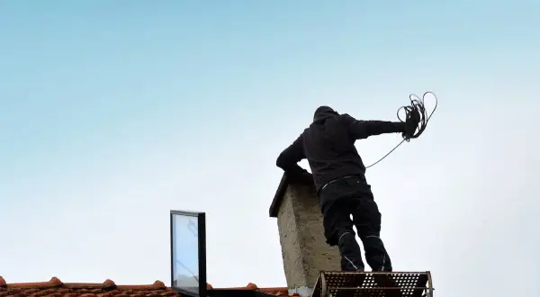 Schornsteinfeger auf dem Dach mit Werkzeug. Was darf der Schornsteinfeger nicht? Er darf nicht ohne Sicherung arbeiten, aber hier ist er gut gesichert.