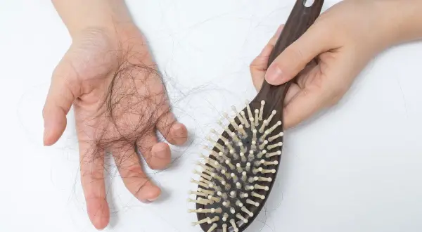Une main tient une brosse à cheveux en bois, tandis que l'autre main montre une perte de cheveux. La lumière rouge met en évidence la perte de cheveux.