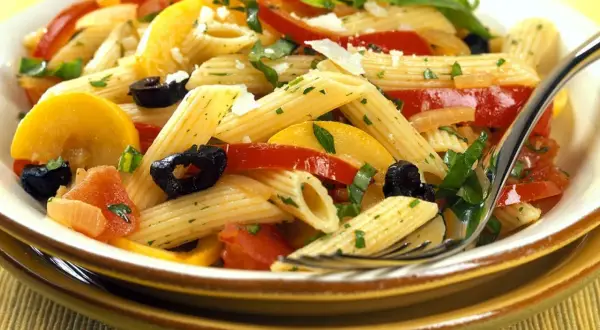 Bunte Nudelgerichte mit Penne, Tomaten, Zucchini, schwarzen Oliven und frischen Kräutern, garniert mit Parmesan.