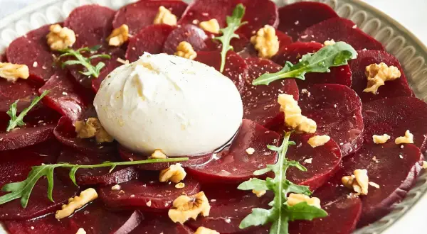 Rote Bete Carpaccio mit Burrata, Walnüssen und Rucola auf einem Teller.
