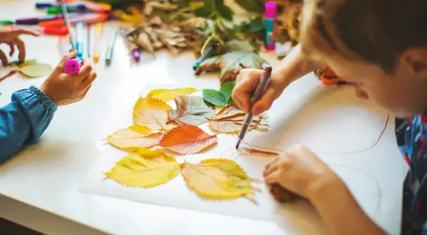 Niños creando arte con hojas de otoño. Actividades para trabajar las plantas en infantil, usando rotuladores y hojas secas para dibujar.