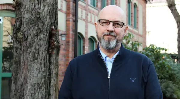 Kaj Stenman, en man med helskägg och glasögon, står framför en tegelbyggnad.