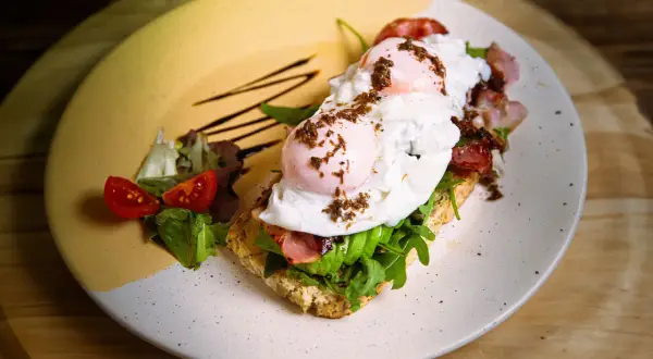 Tostada con aguacate, huevo escalfado y bacon, perfecta para un all day brunch. Acompañada de tomates cherry y rúcula.