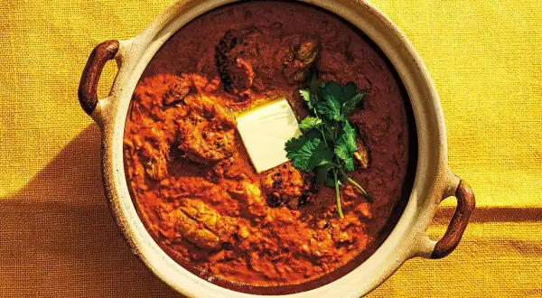En skål med krämig chicken tikka masala, toppad med en smörbit och färsk koriander. Perfekt för en mysig middag.
