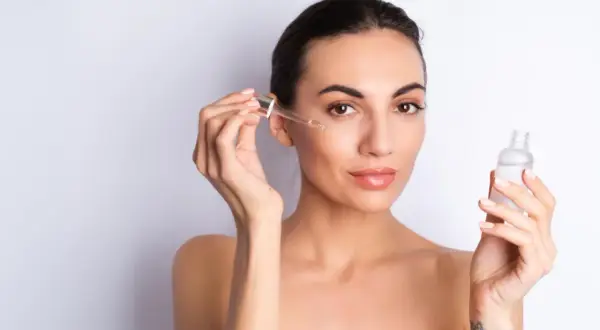 Kobieta aplikuje na twarz serum z peptydami. Skóra wygląda na nawilżoną i promienną.