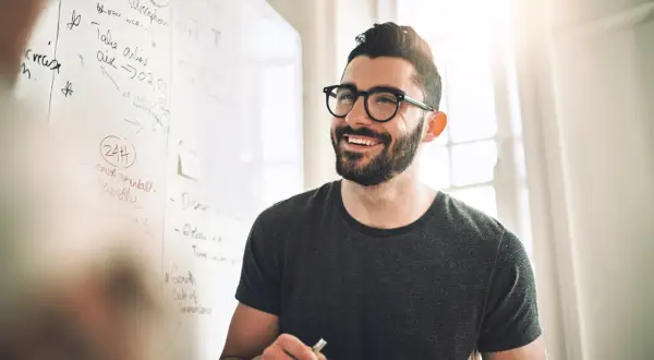 Ein Mann mit Brille lächelt vor einer Tafel mit Notizen zur Fernuni Wirtschaftsinformatik.