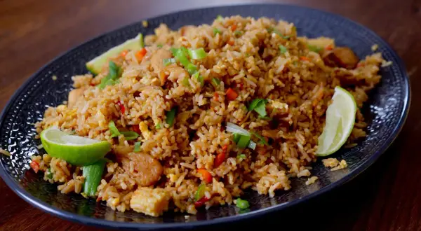 En tallrik med khao pad, en smakrik thailändsk stekt risrätt med kyckling, grönsaker och limeklyftor.