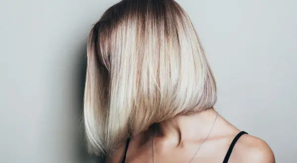 Kobieta z asymetryczną, blond fryzurą typu bob, z ciemniejszymi odrostami.