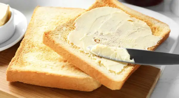 Na desce leżą dwa tosty. Na jednym z nich nóż rozsmarowuje masło. Ile gram ma kromka chleba tostowego?