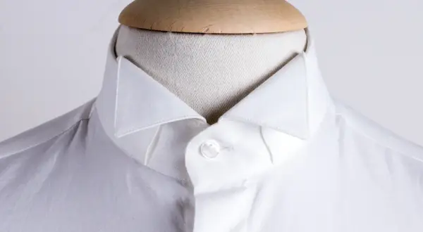 Dettaglio di una camicia bianca da uomo con un elegante camicia con colletto a punta, abbottonata su un manichino.