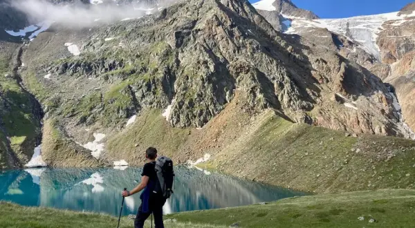 Un randonneur admire un lac turquoise lors d'un trek en Autriche, avec des montagnes imposantes en arrière-plan.