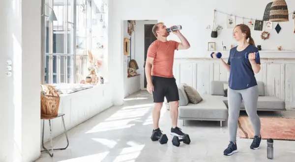 Un homme boit de l'eau pendant que sa compagne fait des exercices avec des haltères, développant ses muscles du bras.