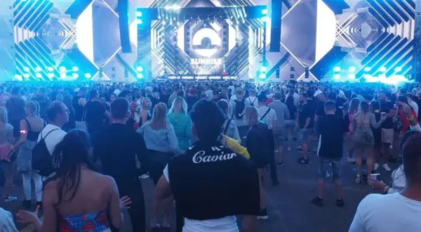 Tłum ludzi na festiwalu Sunrise w Kołobrzegu, podziwiający ogromną scenę z efektami świetlnymi.