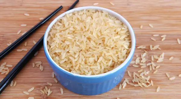 Ein blauer Napf mit hellem Reis, daneben schwarze Stäbchen. Der Unterschied Basmati und Parboiled Reis wird hier visuell dargestellt.