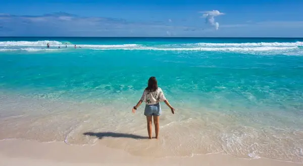 Frau steht im türkisfarbenen Meer, genießt das warme Wetter im Mexiko im Oktober. Der Strand ist sandig, das Wasser klar.