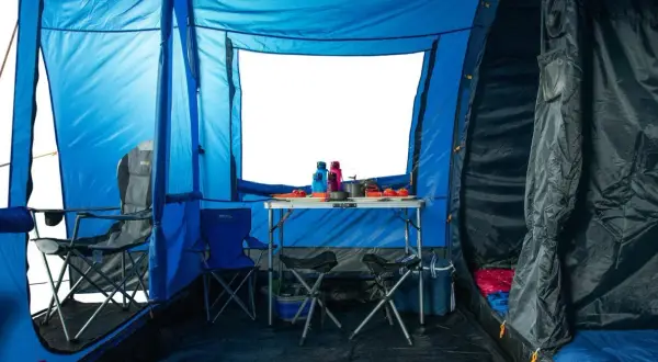 Wnętrze niebieskiego namiotu z rozstawionym stołem, krzesłami i śpiworami. Dobra wodoodporność namiotu zapewnia komfortowe warunki.