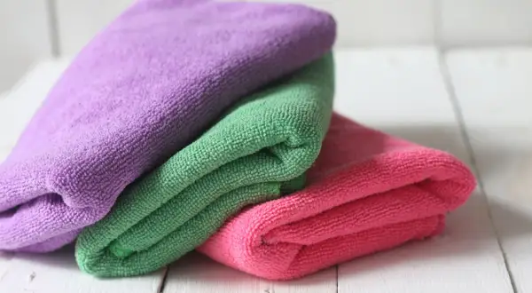 Drei bunte Mikrofasertücher, lila, grün und pink, liegen übereinander. Sie warten darauf, dass man sie zum putzlappen waschen benutzt.