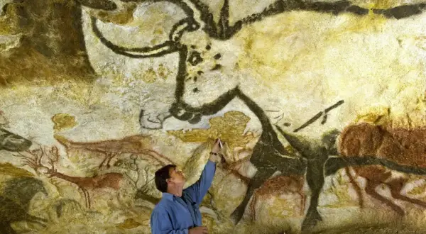 Człowiek bada prehistoryczne malowidła z Lascaux, dotykając pędzlem skalnej ściany z wizerunkami zwierząt.