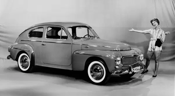 En glad kvinna poserar bredvid en klassisk Volvo PV 444.